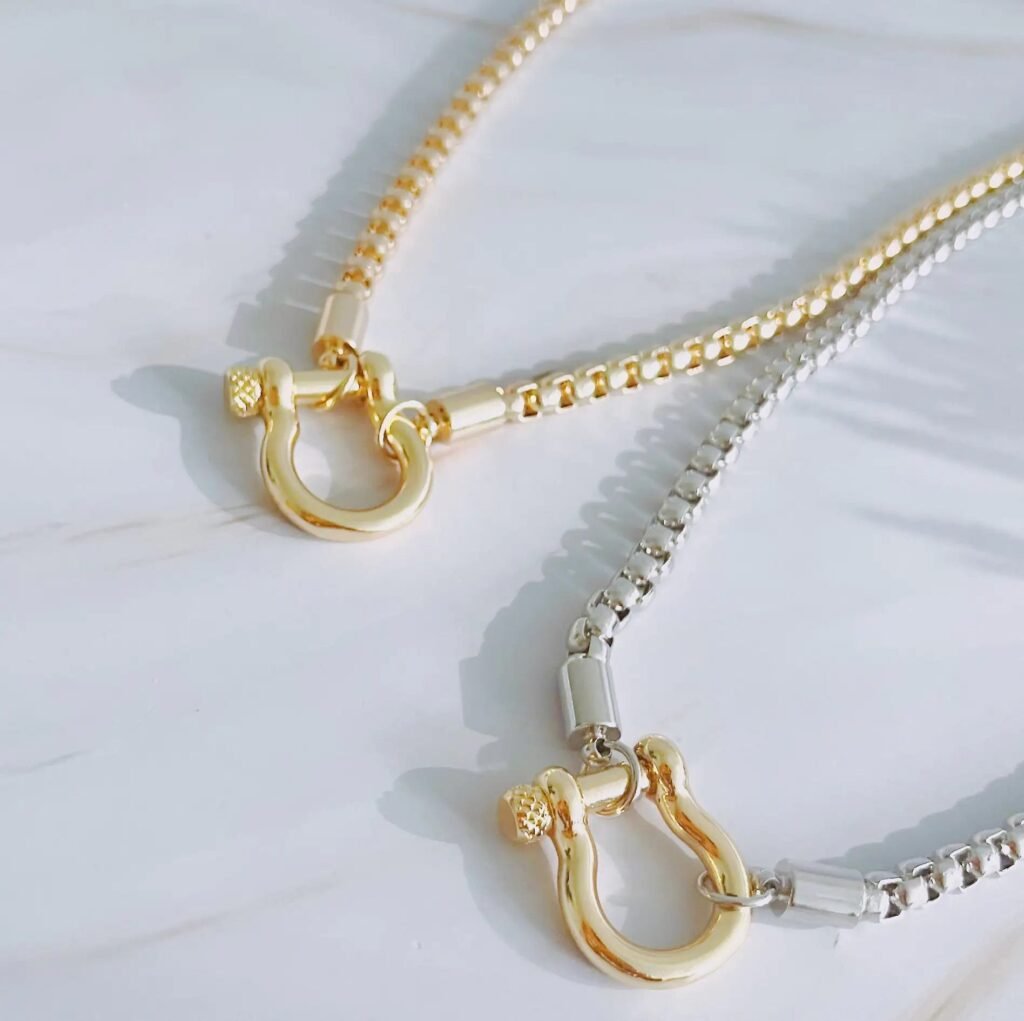 Gold and silver box chain necklaces with shackle pendant on marble