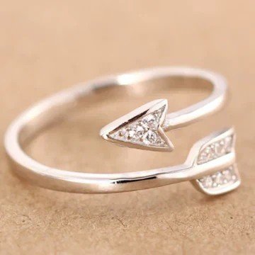 Adjustable silver arrow ring with rhinestones on a beige background